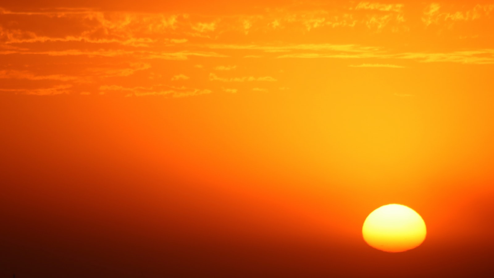 The sun rising over a still horizon in a deep orange sky
