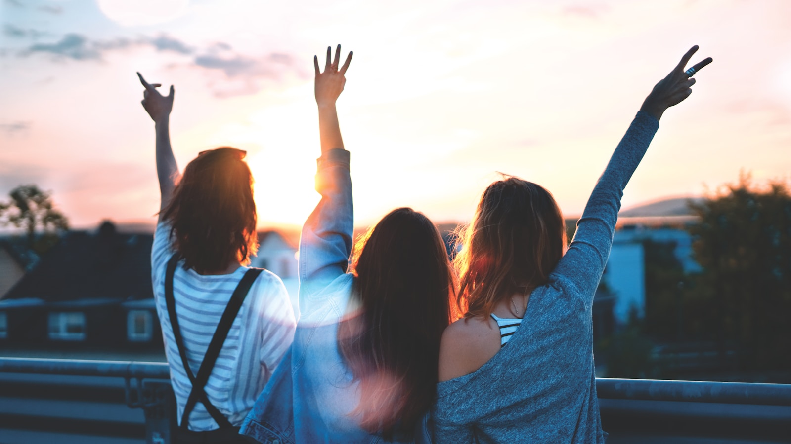 Three friends watching a warm sunset with arms raised in a hopeful gesture