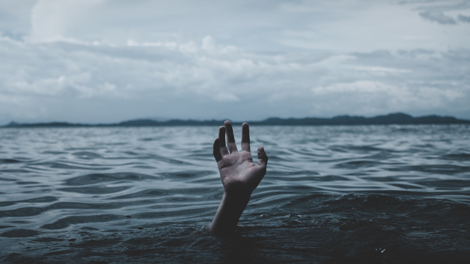 A hand reaching up from open water toward the light above